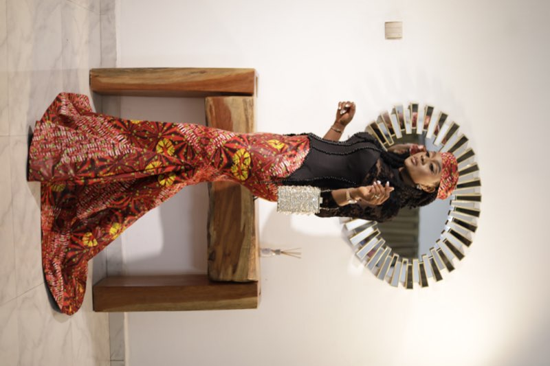 Black lace top and Ankara wrapper dynamic walking pose with crystal clutch by best tailor Enugu
