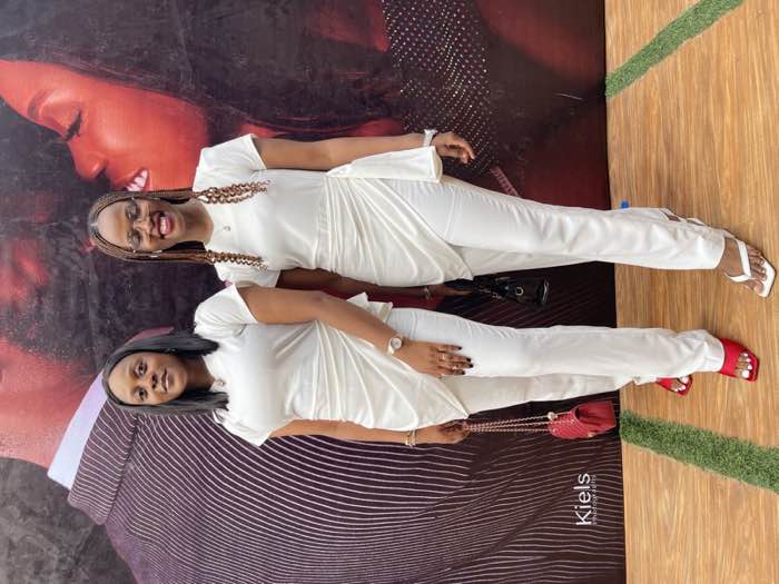 Two women in matching white draped jumpsuits at event by Prom G Fashion Enugu